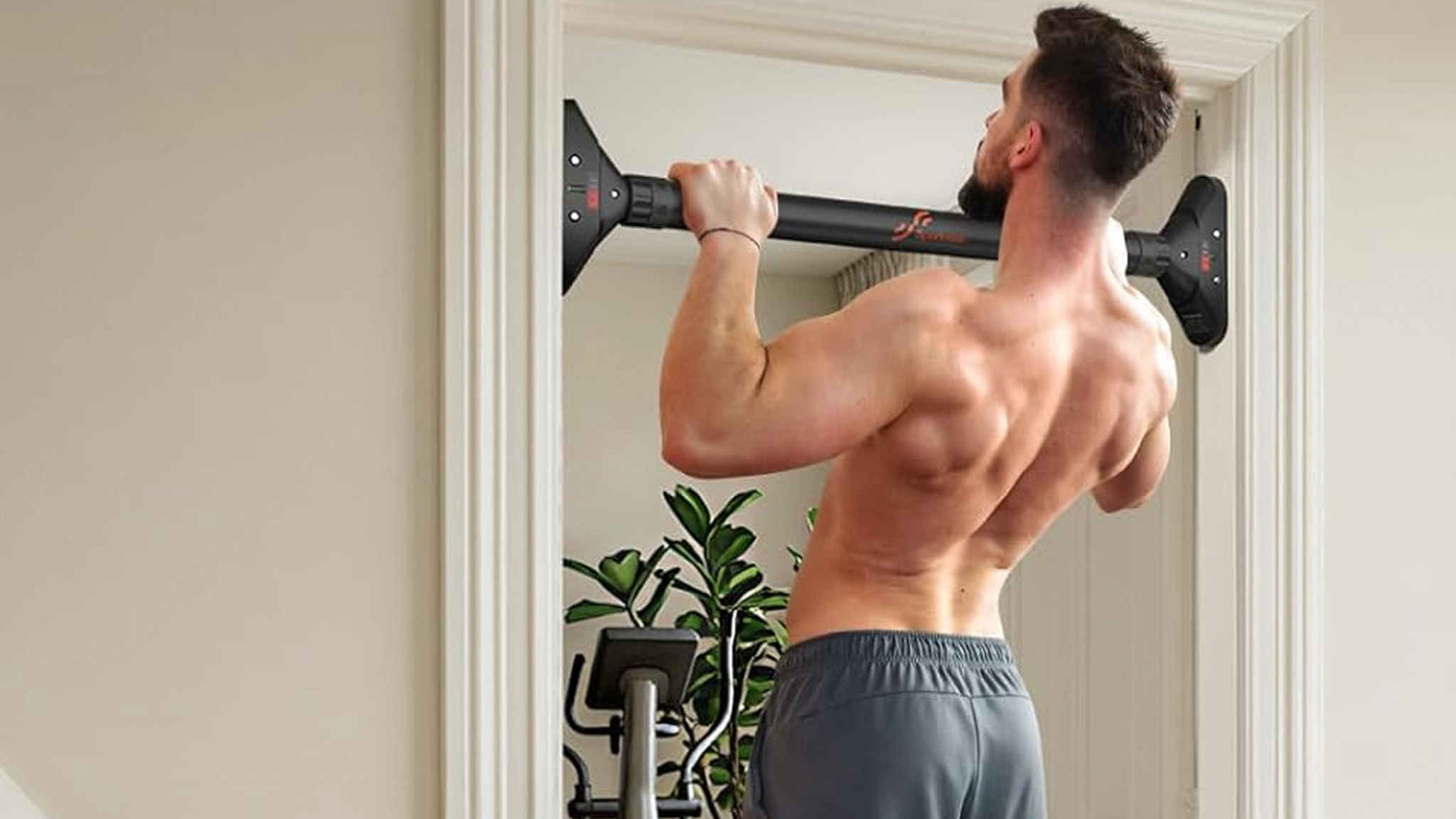 A sportneer pull-up bar being used by a shirtless man in a doorway