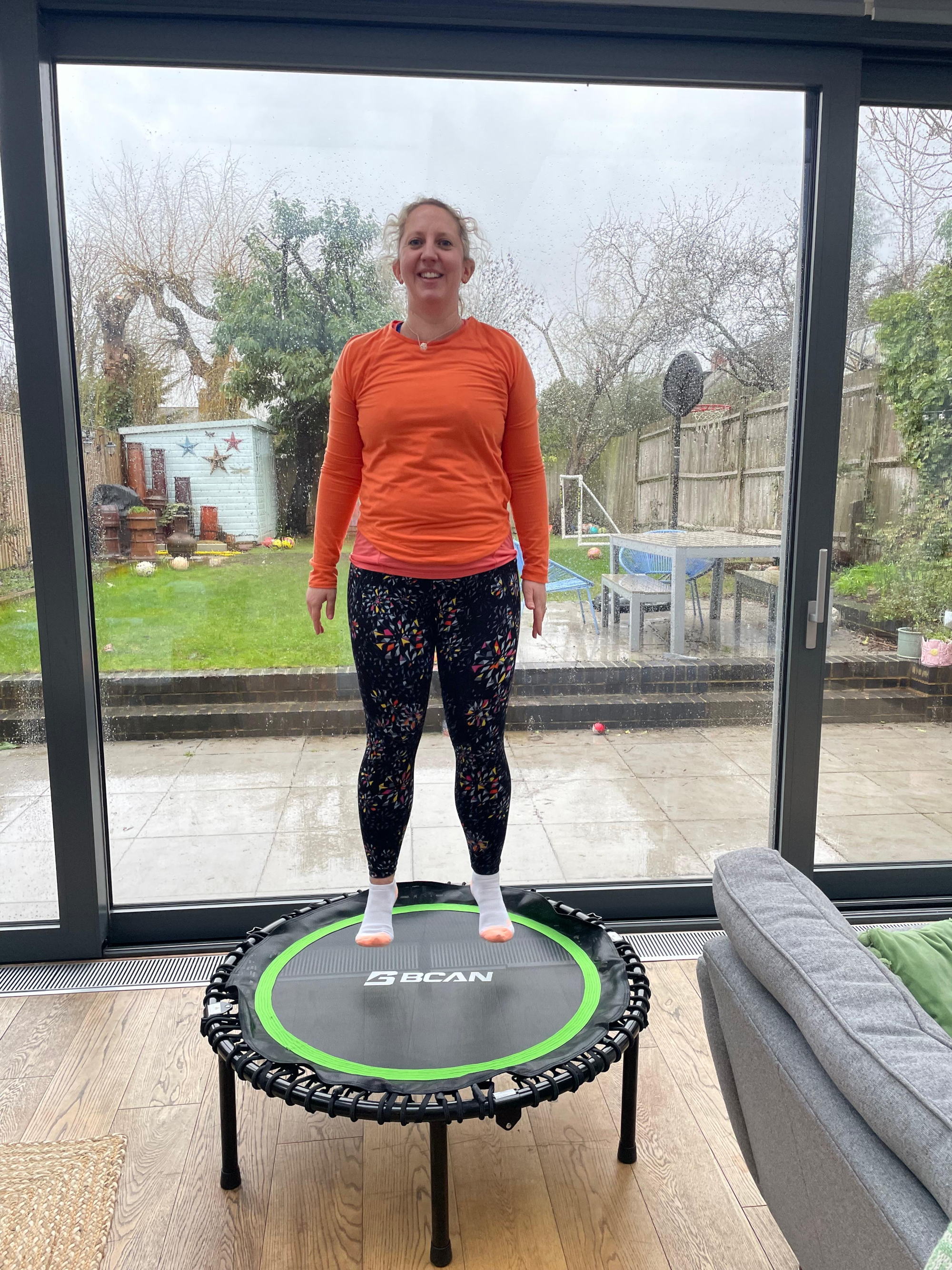 Woman bouncing on small trampoline in domestic setting, a view of a small garden is seen through patio doors