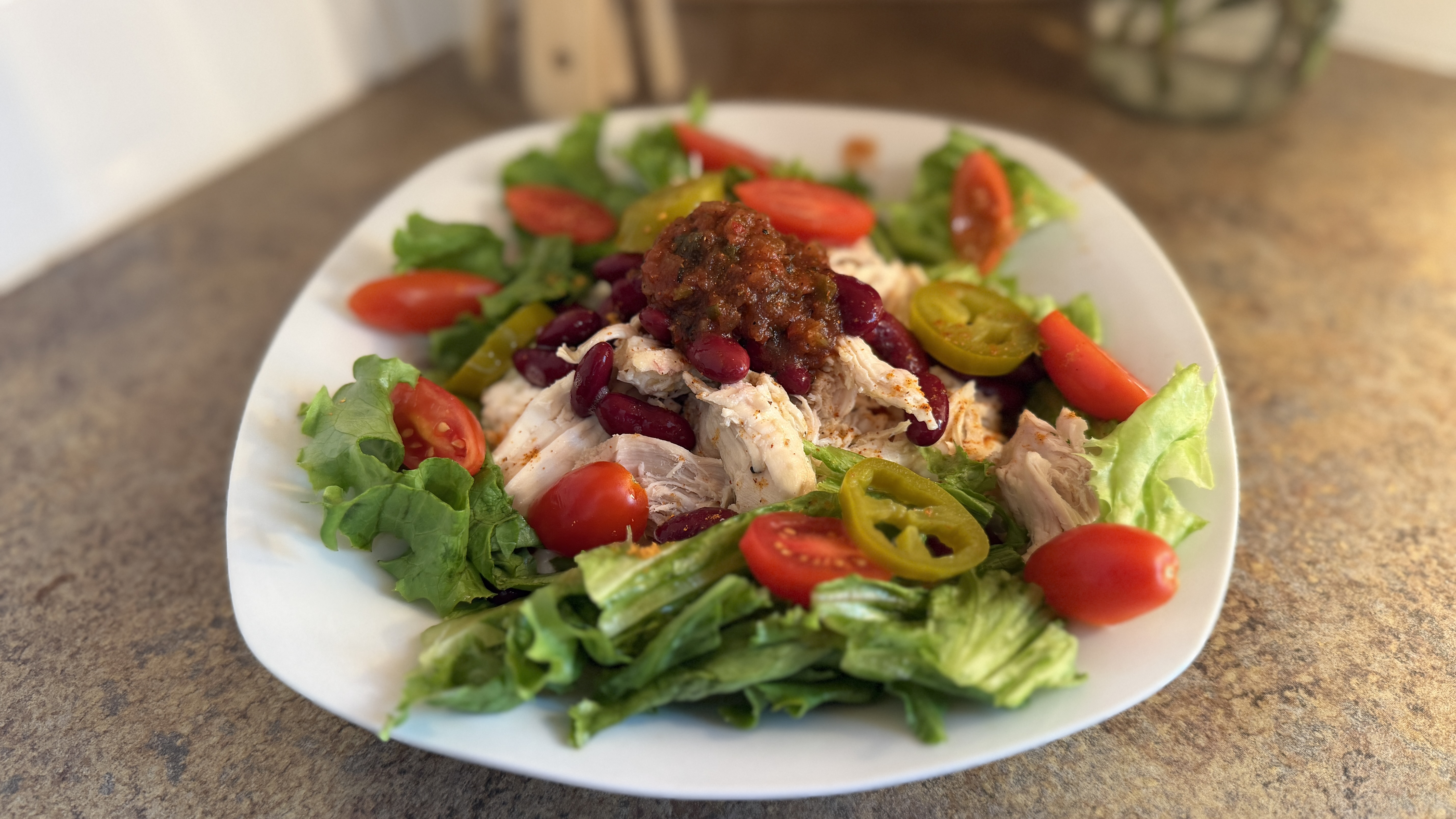 Plate of salad, with bed of lettuce topped with ingredients including cherry tomatoes, chicken, and jalapeñoes
