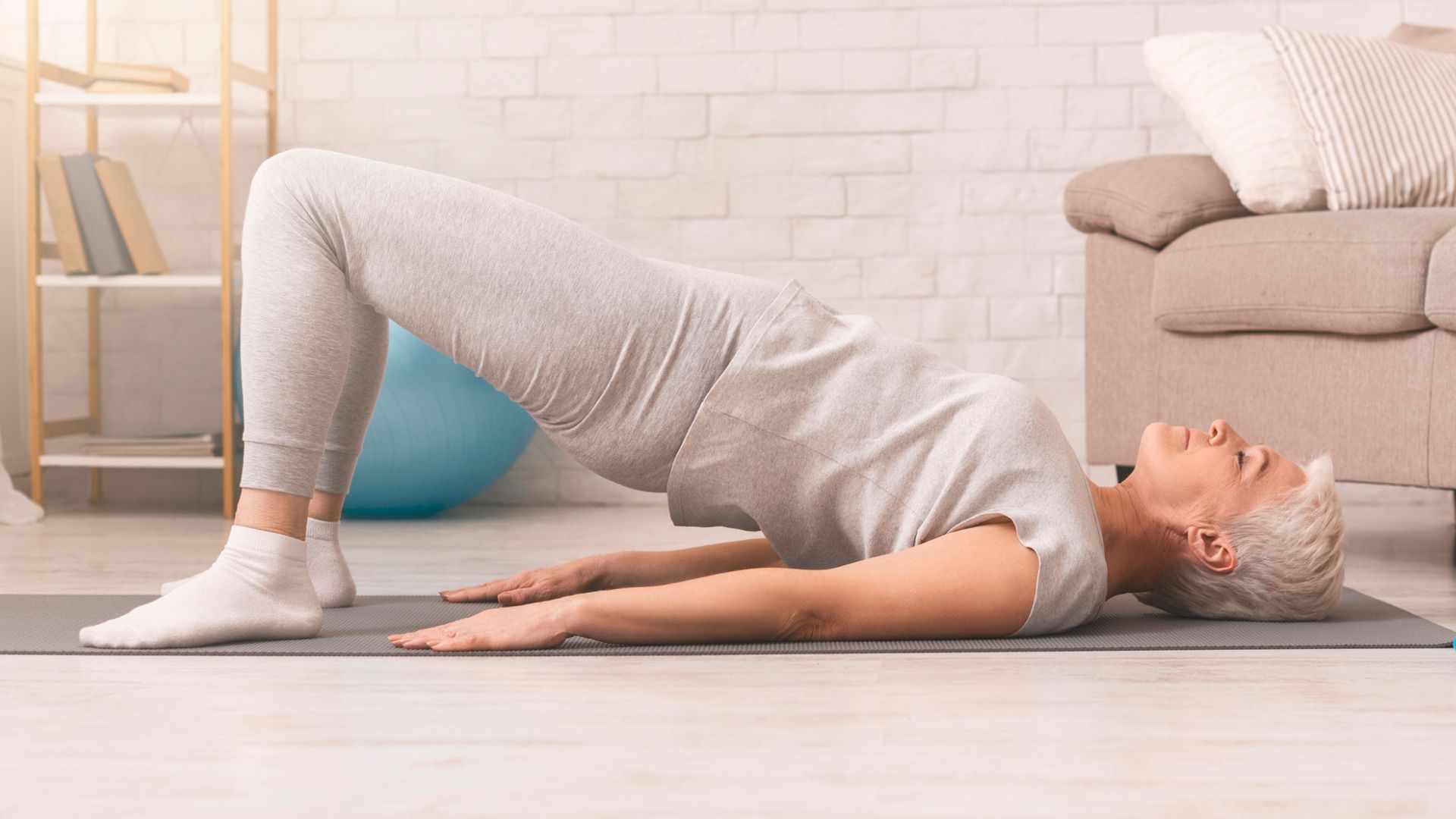 Senior woman does a glute bridge exercise on a yoga mat