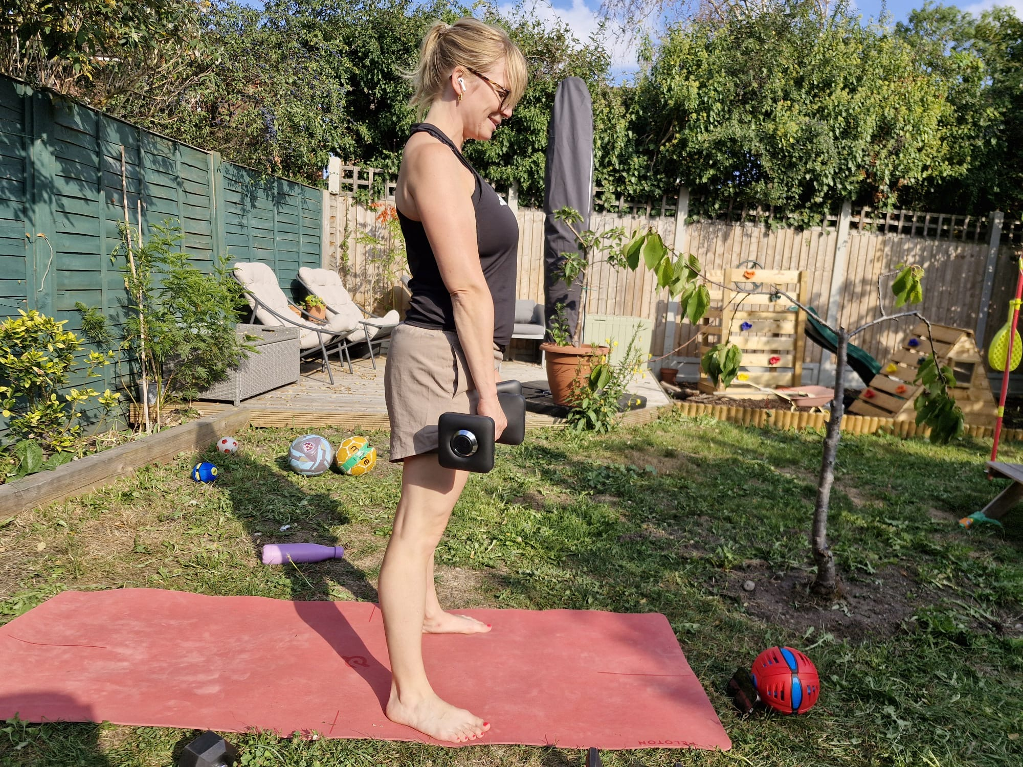 Woman stands in garden holding dumbbells